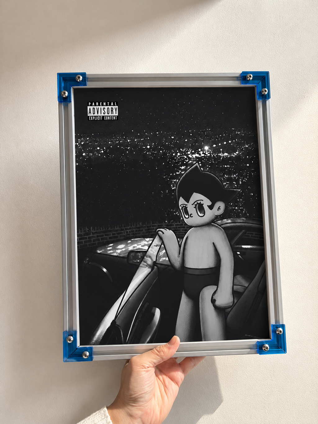 Hand holding a silver-colored frame with blue corners, displaying black-and-white Astro Boy artwork with a car.