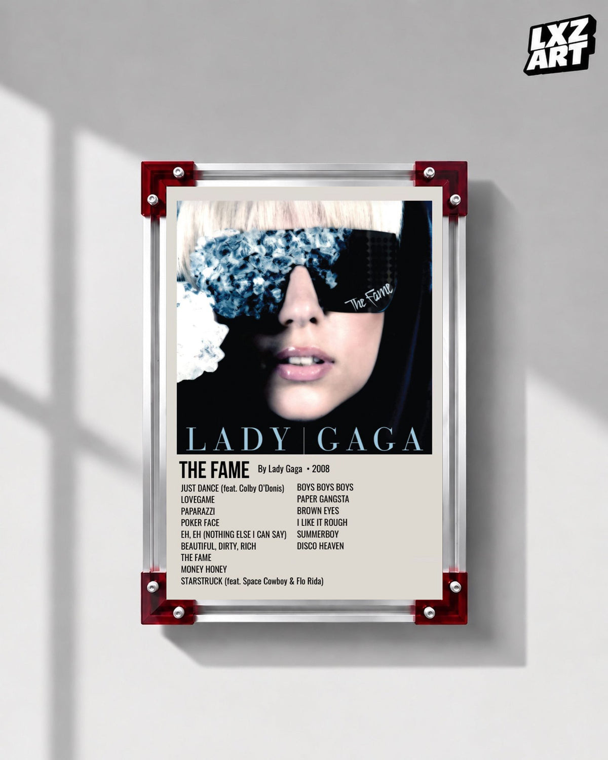 Lady Gaga The Fame tracklist poster displayed on a gray wall in a red corner frame; unframed print, frame not included