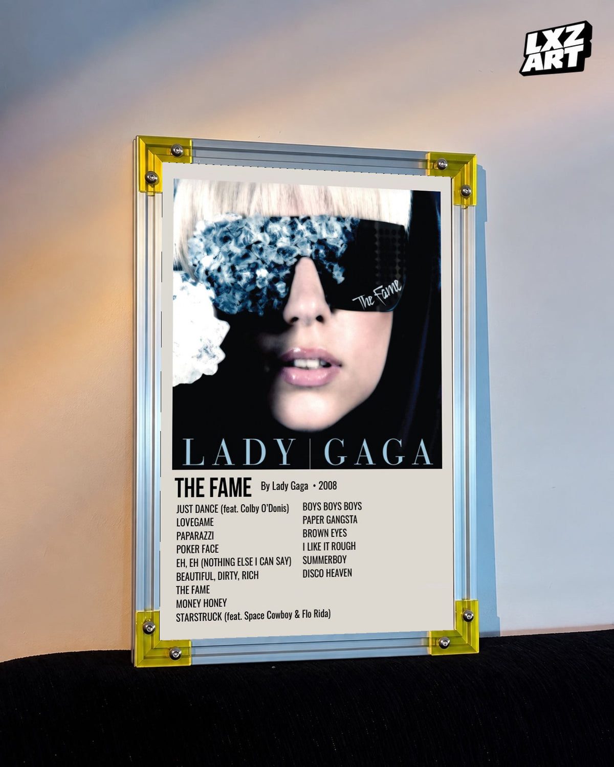 Lady Gaga The Fame tracklist poster displayed against a warm wall in a yellow corner frame; unframed print, frame not included