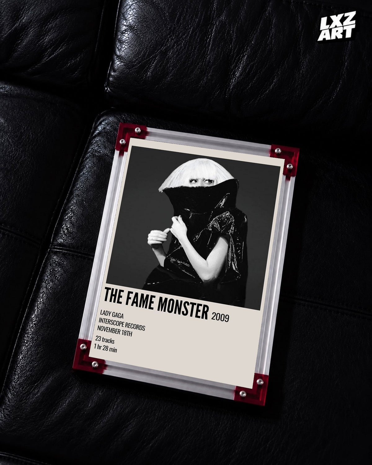 Lady Gaga The Fame Monster album cover poster displayed on a black leather sofa in a red corner frame; unframed print, frame not included