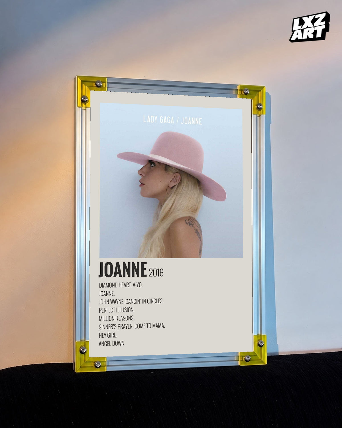 Lady Gaga Joanne tracklist poster displayed against a warm wall in a yellow corner frame; unframed print, frame not included