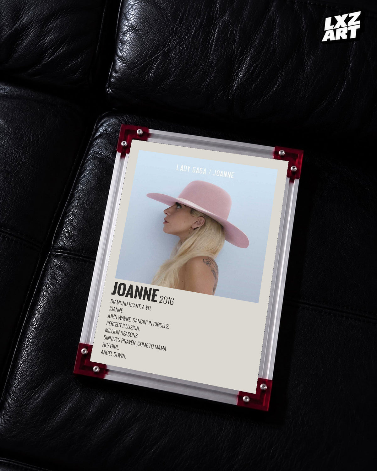 Lady Gaga Joanne tracklist poster displayed on a black leather sofa in a red corner frame; unframed print, frame not included