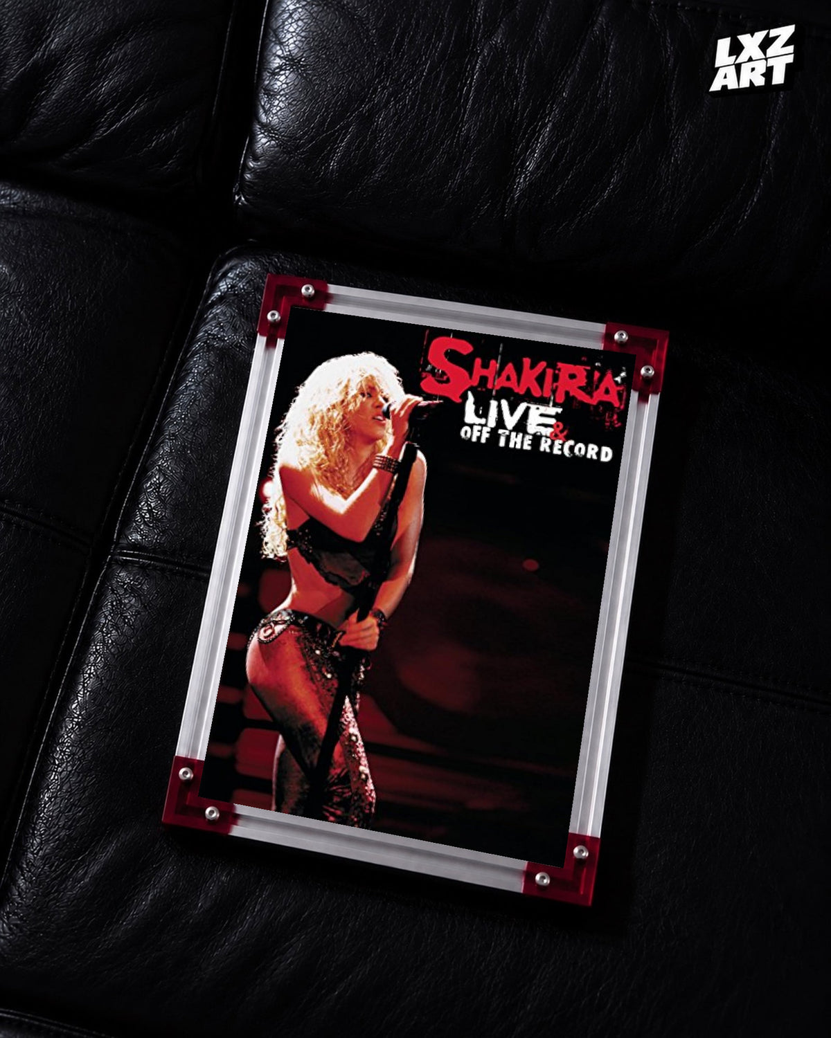 Shakira Live & Off the Record concert film poster displayed on a black leather sofa in a red corner frame; unframed print, frame not included