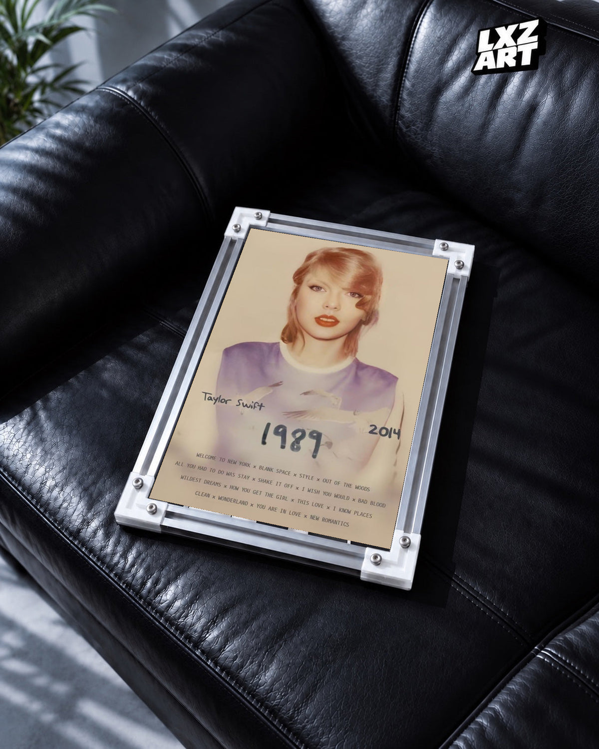 Taylor Swift 1989 Deluxe Edition Poster in white-corner frame on black leather sofa. Frame shown for display only.