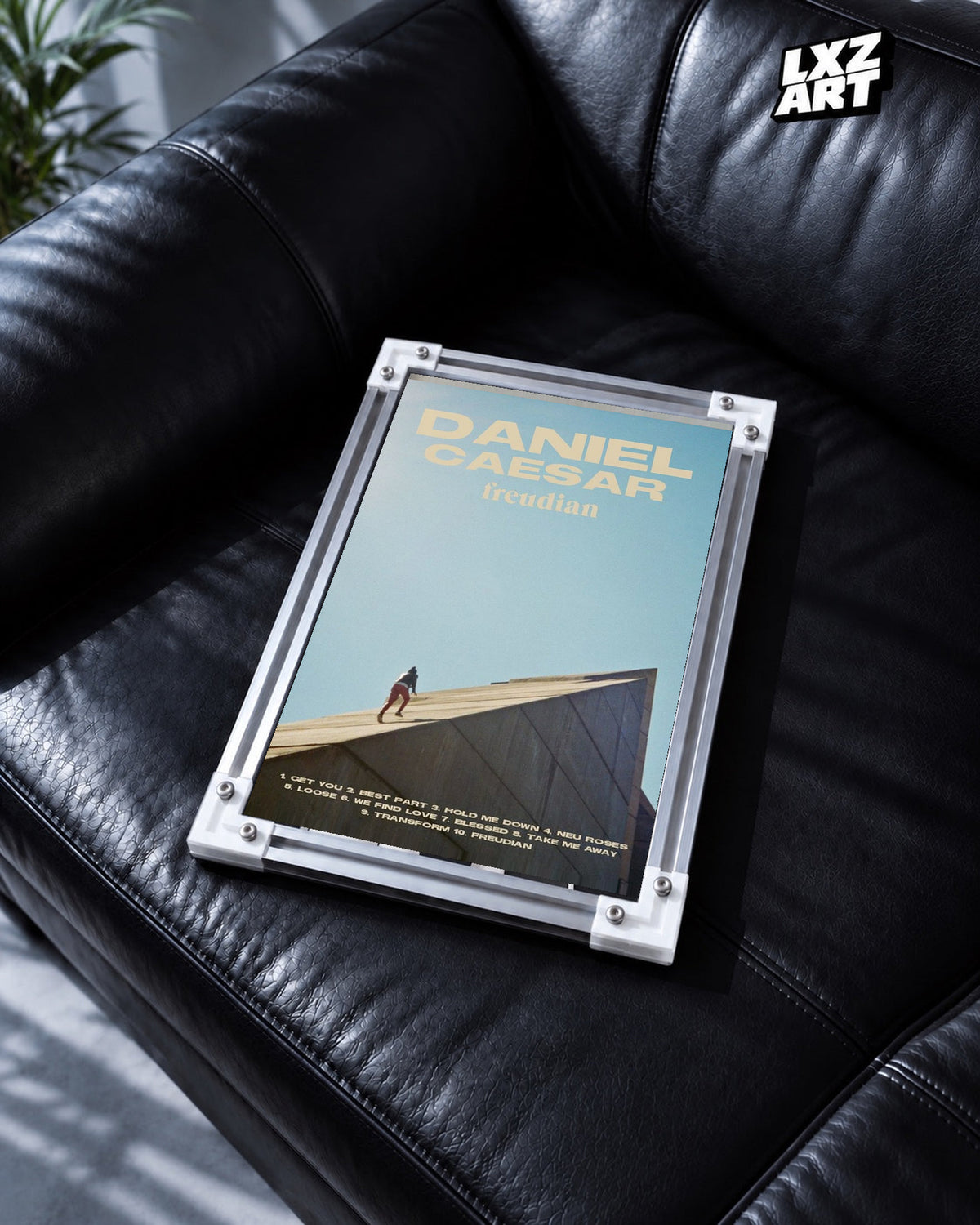 Daniel Caesar Freudian Sky Blue Album Poster in white-corner frame on black leather sofa. Frame shown for display only.