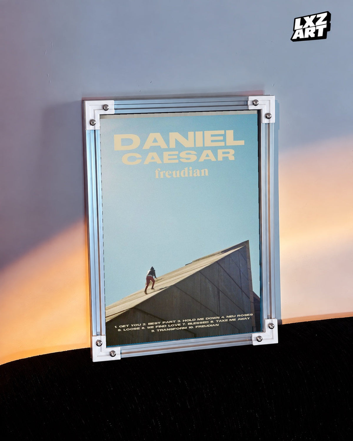 Daniel Caesar Freudian Sky Blue Album Poster in white-corner frame beside warm-lit wall. Frame shown for display only.