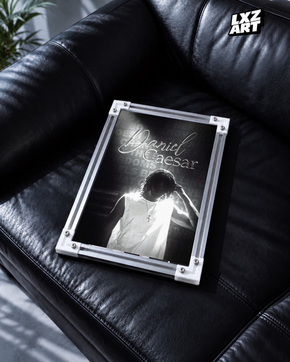 Daniel Caesar Black & White Backlit Portrait Poster in white-corner frame on black leather sofa. Frame shown for display only.