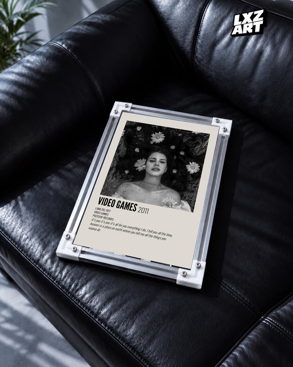 Lana Del Rey Video Games Monochrome Floral Portrait Poster in white-corner frame on black leather sofa. Frame shown for display only.