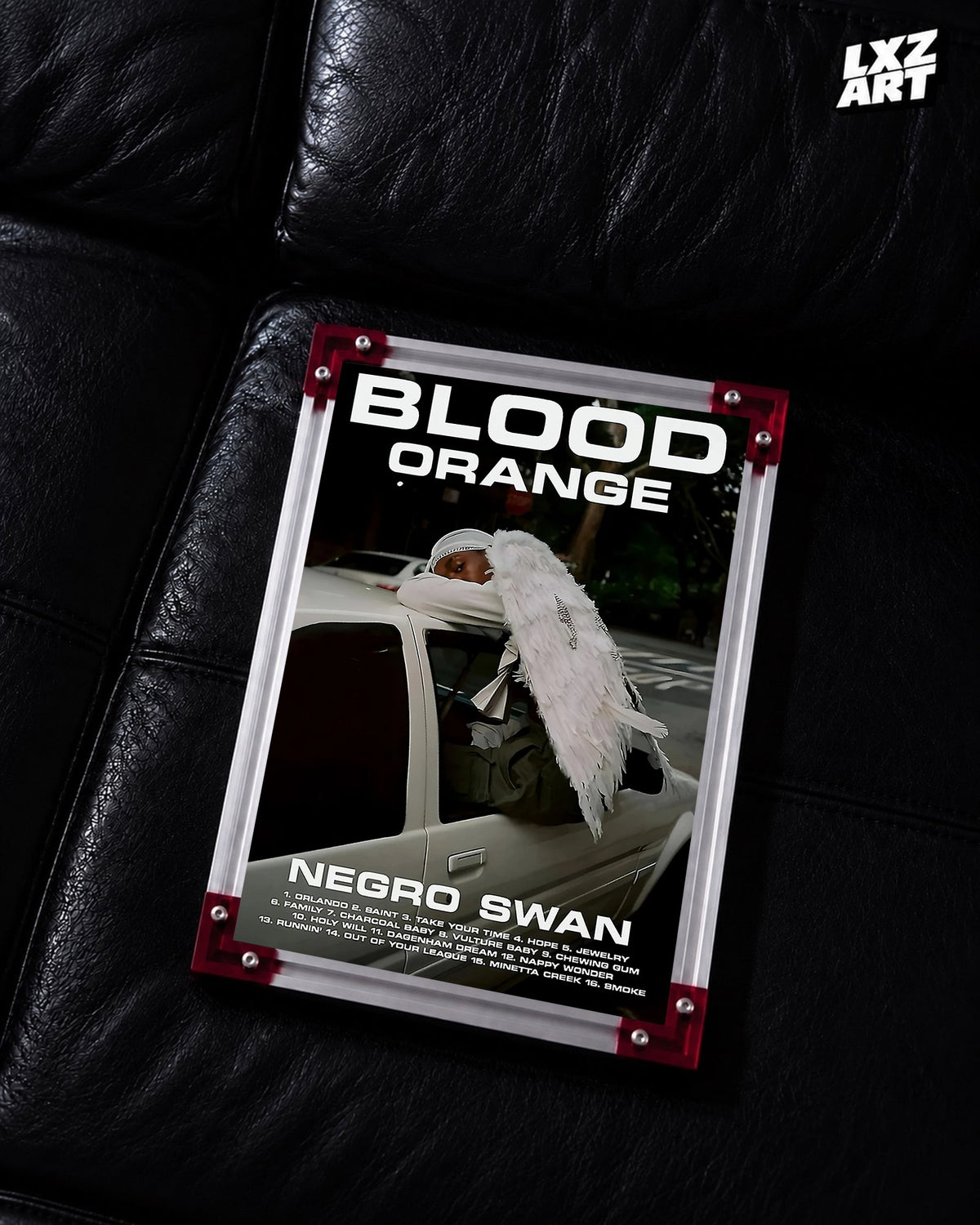 Blood Orange Negro Swan bold white type poster displayed on a black leather sofa in the red-corner frame; unframed print, frame not included