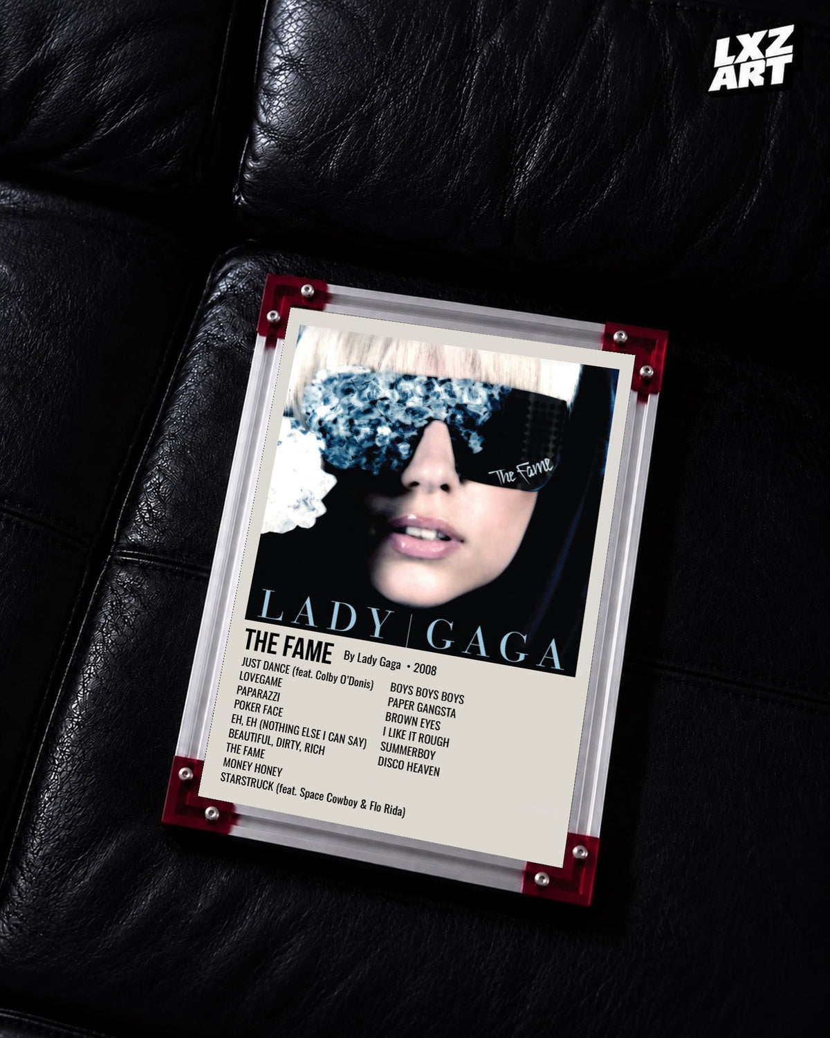 Lady Gaga The Fame tracklist poster displayed on a black leather sofa in a red corner frame; unframed print, frame not included