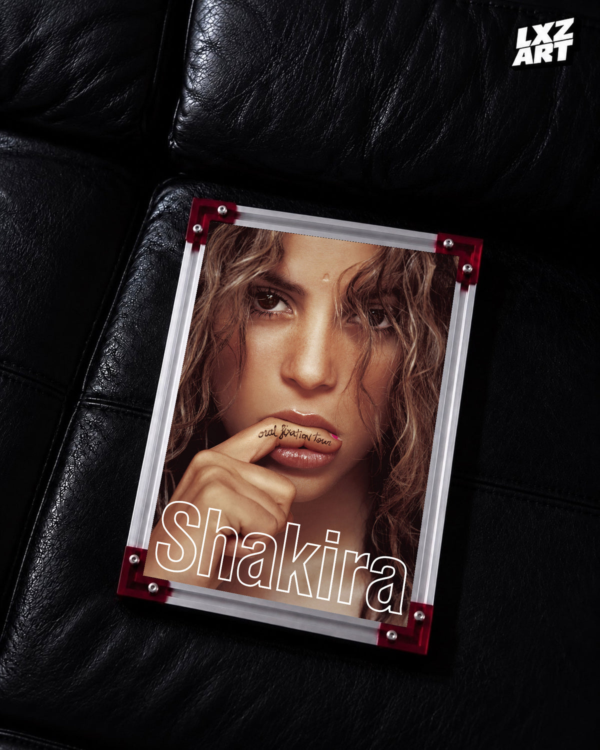 Shakira Oral Fixation Tour concert film poster displayed on a black leather sofa in a red corner frame; unframed print, frame not included