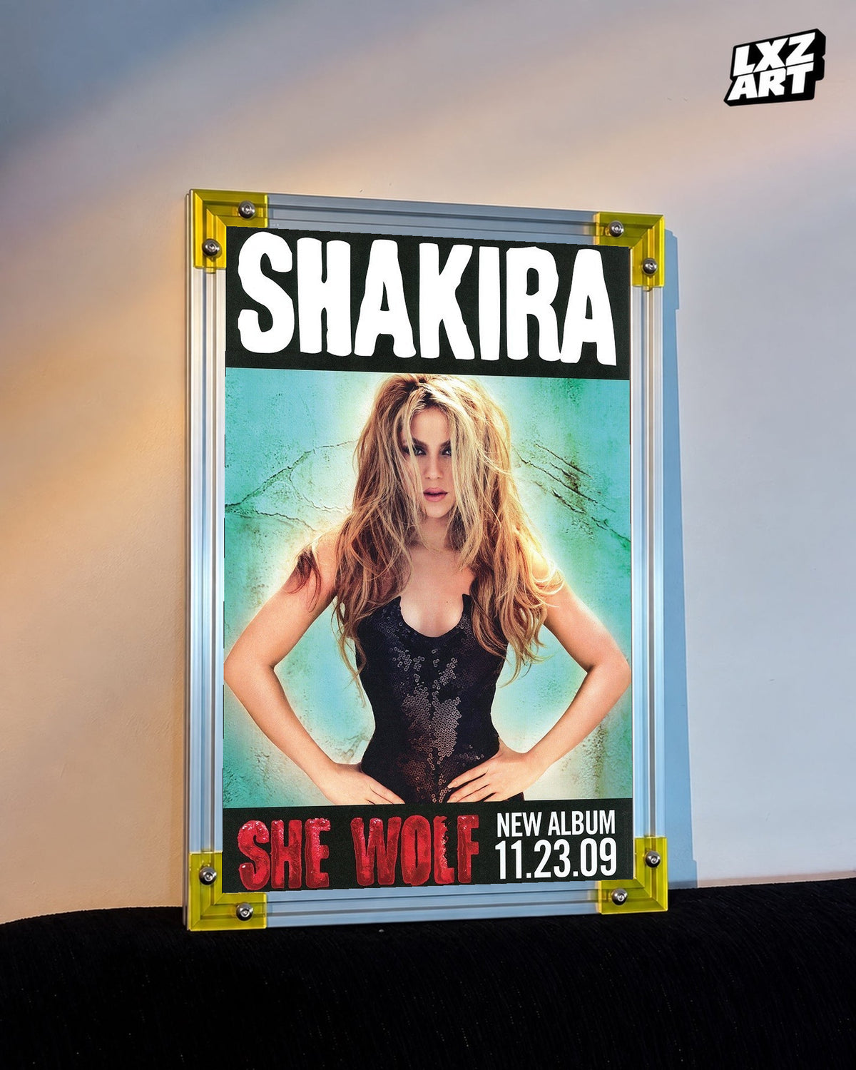 Shakira She Wolf album promo poster displayed against a warm wall in a yellow corner frame; unframed print, frame not included