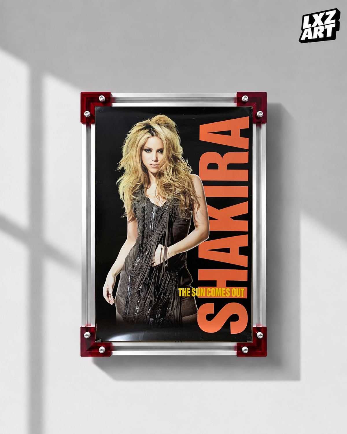 Shakira The Sun Comes Out World Tour concert tour poster displayed on a gray wall in a red corner frame; unframed print, frame not included