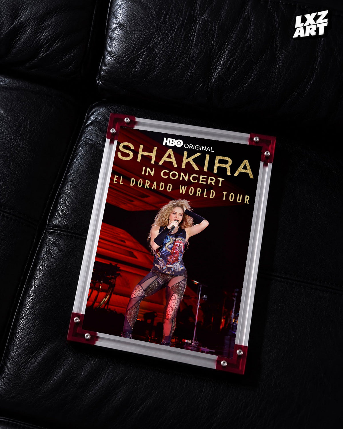 Shakira In Concert: El Dorado World Tour concert film poster displayed on a black leather sofa in a red corner frame; unframed print, frame not included