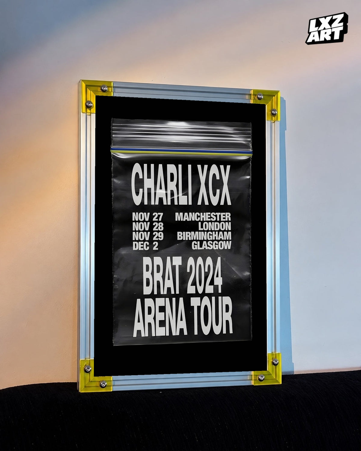 Charli xcx Brat 2024 UK Arena Tour Zip Bag Poster displayed on a warm wall in a yellow corner frame; unframed print, frame not included